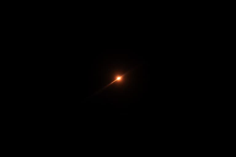 A tiny ember-orange point of light streaking through pure black space, leaving one long thin straight trail behind it